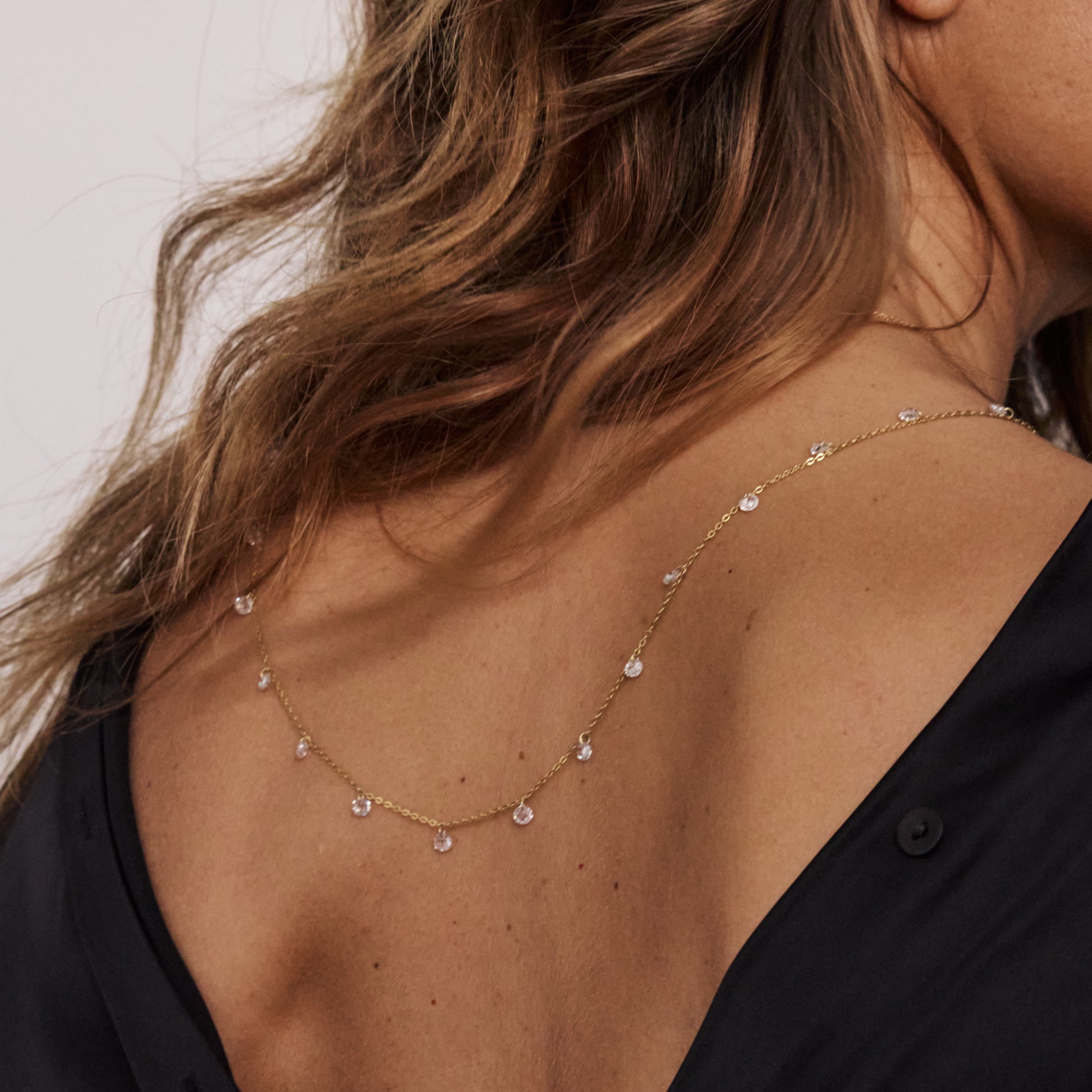 Detalhe de colar em prata banhada a ouro com cristais transparentes sobre vestido preto.