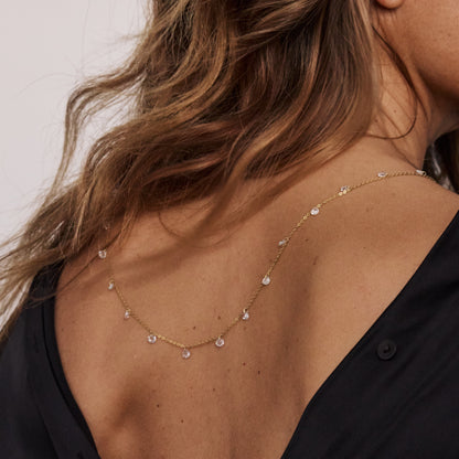 Detalhe de colar em prata banhada a ouro com cristais transparentes sobre vestido preto.